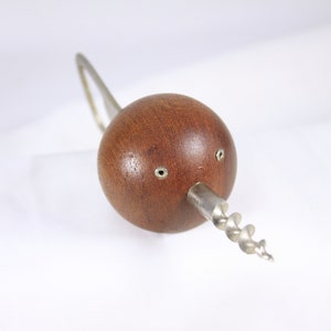 May include: A wooden corkscrew with a spherical handle and a silver metal spiral. The handle is a dark brown color with two small silver rivets. The corkscrew has a silver metal loop.