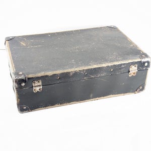 May include: A rectangular black storage box with a worn, distressed finish. The box features silver-toned metal corner protectors and two silver-toned metal hinges along the front edge. The surface shows visible signs of age and wear throughout.