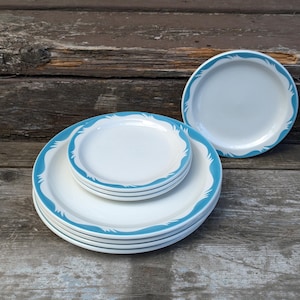 May include: A collection of white ceramic plates featuring a blue wave pattern around the edge. The plates are in different sizes, with smaller ones stacked on a larger plate. One plate is shown separately.