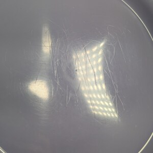 May include: A close-up of a light purple disc with a white rim. The disc has a series of scratches and marks on its surface.