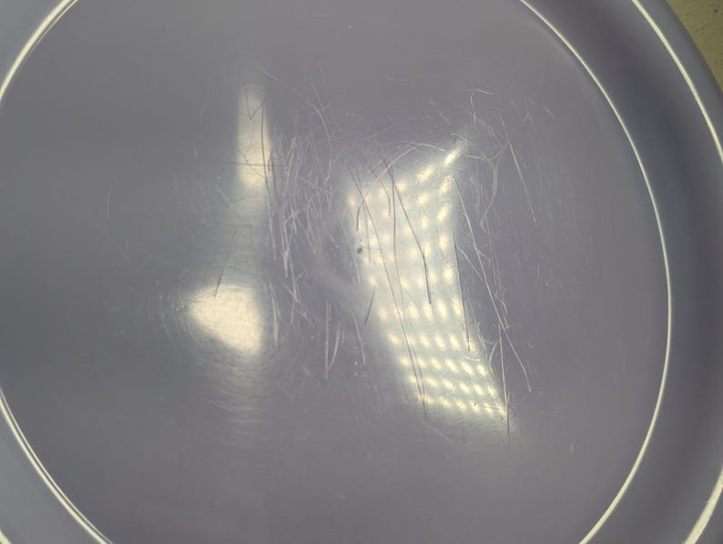 May include: A close-up of a light purple disc with a white rim. The disc has a series of scratches and marks on its surface.