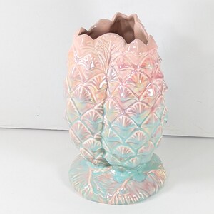 以下が含まれることがあります： パステルカラーのセラミックパイナップル型花瓶。ピンクからブルーに変化し、イリデセントなハイライトがあります。ベースと内側は濃いピンク色です。花瓶はテクスチャード加工された表面を持っています。