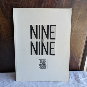 Peut inclure: Une couverture de livre blanche avec le titre "NINE BY NINE" en texte noir. La couverture liste également les photographes : David Bailey, Erich Salomon, Cecil Beaton, Anne Leibovitz, Don McCullin, Helmut Newton et Alice Springs.