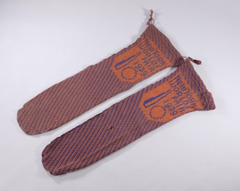 May include: Two vintage knitted socks in shades of brown and blue. Each sock features a design with the text "NEW YORK WORLD'S FAIR 1939" in blue and orange. The socks have a textured pattern and a tassel at the top.
