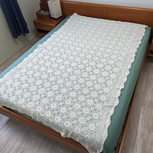 May include: A white crocheted bedspread with a delicate floral pattern. The bedspread is on a wooden bed frame with a teal blue mattress.