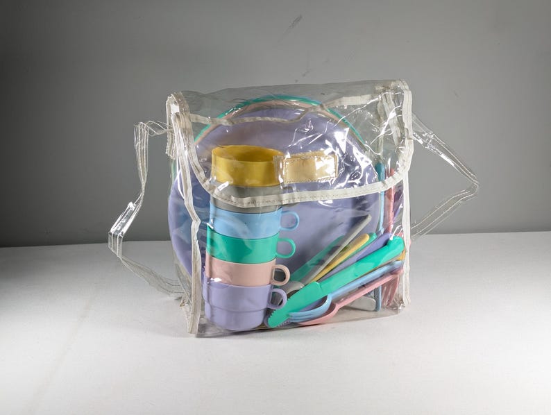 May include: A clear plastic bag containing a set of colorful plastic plates, cups, and utensils. The set is designed for children and is perfect for picnics or outdoor play.