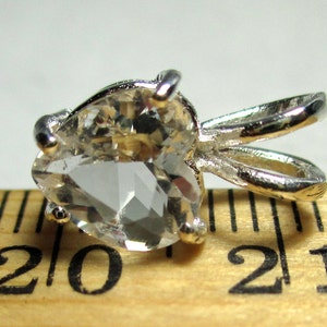 May include: A silver pendant with a clear heart-shaped crystal. The pendant is about 2 inches long and is sitting on a wooden ruler.