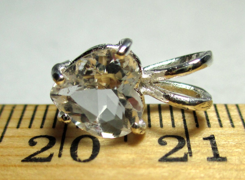 May include: A silver pendant with a clear heart-shaped crystal. The pendant is about 2 inches long and is sitting on a wooden ruler.