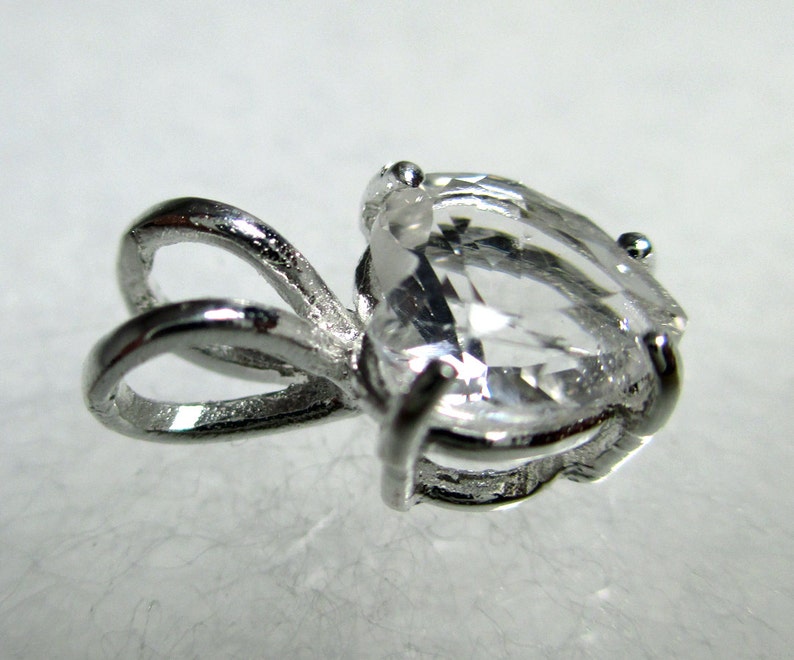 May include: A silver pendant with a clear pear-shaped gemstone. The pendant has a bail with a loop for attaching a chain.