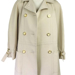 May include: A beige trench coat with gold-colored buttons and accents. The coat features a double-breasted design, a notched collar, and a belt detail on the sleeves. The coat is displayed on a mannequin.