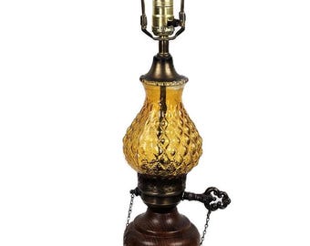 May include: Vintage table lamp with a brass base and accents, a dark wood center, and a textured amber glass shade. The lamp has a decorative pull chain and a metal lamp shade holder.