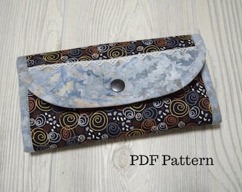 May include: A black and brown fabric wallet with a blue and white fabric flap. The flap has a white lace trim and a black button. The wallet is closed and lying on a light wood surface. PDF Pattern.