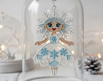May include: A whimsical Christmas ornament featuring a doll-like figure with a snowflake headdress and dress, displayed under a glass cloche. The ornament has blue and white details, and is suspended from a snowy branch. The base is white, and the background is softly lit.