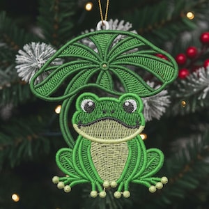 May include: Embroidered frog ornament in shades of green, with a lily pad above its head. The frog has large eyes and a smiling expression. The ornament is hanging from a gold string, perfect for a Christmas tree.