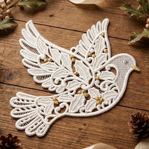 Op de afbeelding: Een witte kanten duifversiering met ingewikkelde details, met hulst- en bessenaccenten. De duif heeft een gouden snavel en ligt op een houten achtergrond met linten en dennenappels, perfect voor feestelijke decoratie.