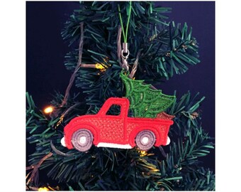 Pode incluir: Caminhão vermelho com uma árvore de Natal verde na caçamba, pendurado em uma árvore de Natal. O caminhão é um enfeite de Natal.