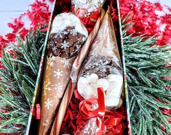 May include: A festive tin filled with a hot chocolate mix, marshmallows, chocolate chips, and a candy cane. The tin is decorated with a Christmas theme and is filled with red and white tissue paper.
