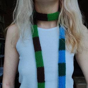 May include: Two knitted scarves, one green and brown, the other blue and green, are worn around the neck of a person with long blonde hair.