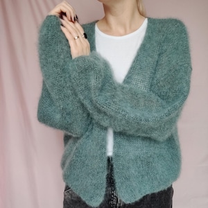 May include: A soft, light green cardigan with a V-neck and long sleeves. The cardigan is made of a fuzzy, mohair-like yarn.