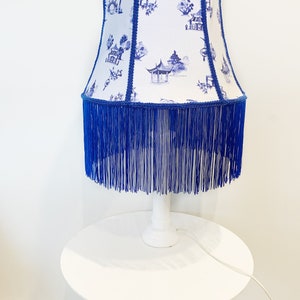 Blue and white fabric lampshade with Japanese pagodas and blue fringe, lampshade stand, tabletop.