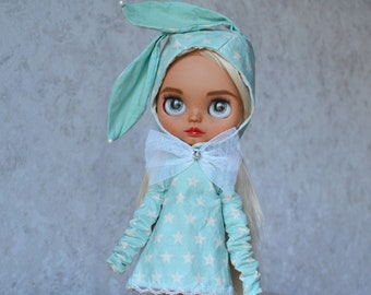 Puede incluir: Una muñeca con un disfraz de conejito azul claro con estrellas blancas y un lazo blanco. La muñeca tiene el pelo rubio y los ojos azules.