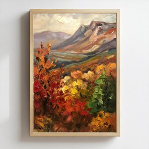 May include: An oil painting in a light wood frame depicts a mountain landscape. The foreground features vibrant autumn foliage in shades of red, orange, yellow, and green. The background shows mountains under a cloudy sky, with a palette of browns, blues, and purples.