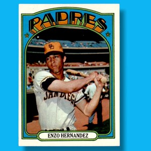 May include: A vintage baseball card featuring Enzo Hernandez of the San Diego Padres. The card has a blue border with the team name in orange and yellow. Hernandez is shown in his Padres uniform, holding a bat.