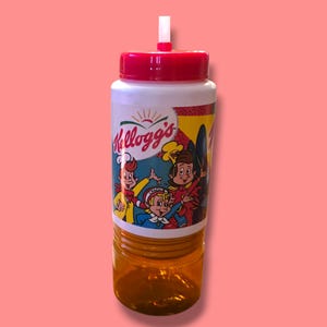 May include: A clear plastic water bottle with a red lid and straw. The bottle features a Kellogg's logo and cartoon characters. The bottom half of the bottle is amber-colored.