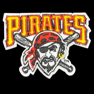 May include: Embroidered patch featuring the word "PIRATES" in yellow and orange, with a pirate logo below. The pirate has a red bandana, an eye patch, and crossed baseball bats. The patch has a white border.