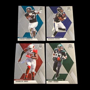 Könnte beinhalten: Vier Football-Sammelkarten mit den Spielern Leonard Fournette, Marquise Brown, Chandler Jones und Jamal Adams. Jede Karte hat ein Mosaikdesign mit Spielerbildern und Teamnamen. Die Karten befinden sich auf einem schwarzen Hintergrund.