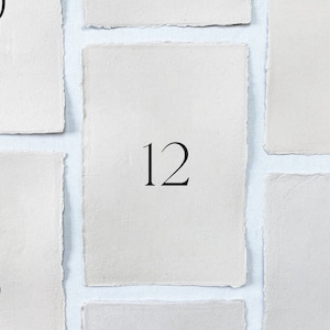 May include: Close-up of four white paper squares with numbers 10, 11, 12, and 14 printed on them.