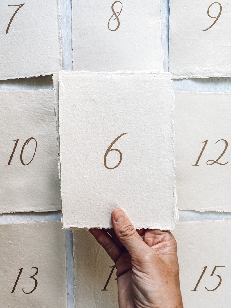 May include: A hand holds up a white card with the number "6" written on it. The card is surrounded by other white cards with numbers 7, 8, 9, 10, 12, 13, 14, and 15 written on them.
