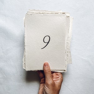May include: A stack of handmade paper with the number 9 written in black ink.