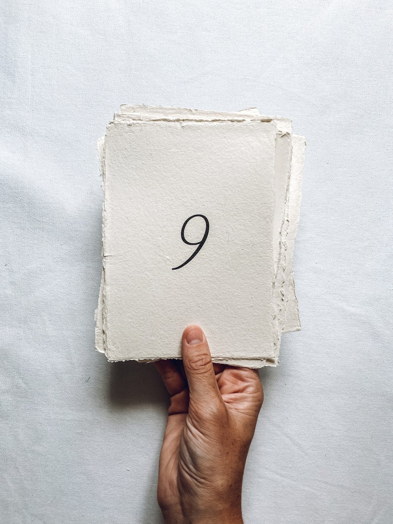 May include: A stack of handmade paper with the number 9 written in black ink.