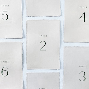 May include: Six white table number cards with black text. The cards are numbered 2, 3, 4, 5, and 6. Each card has the word "TABLE" above the number.