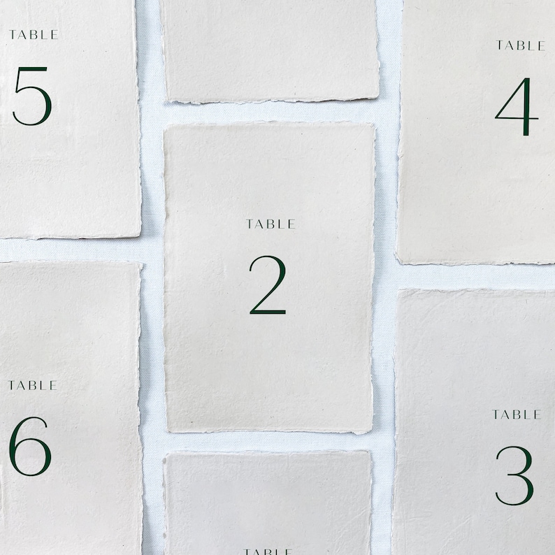 May include: Six white table number cards with black text. The cards are numbered 2, 3, 4, 5, and 6. Each card has the word "TABLE" above the number.