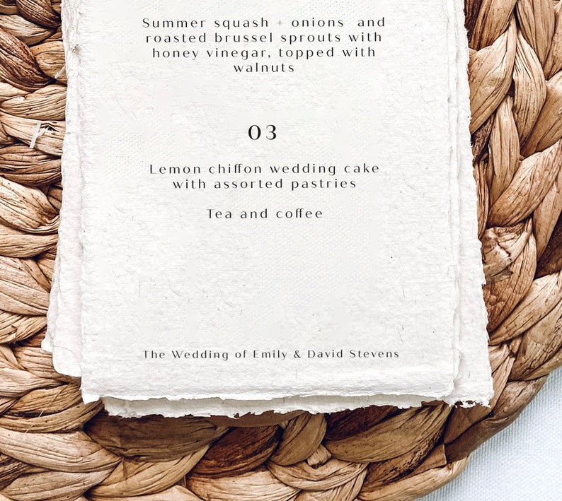 K&ouml;nnte beinhalten: Eine wei&szlig;e Karte mit dem Text "Summer squash + onions and roasted brussel sprouts with honey vinegar, topped with walnuts" und "03 Lemon chiffon wedding cake with assorted pastries Tea and coffee The Wedding of Emily & David Stevens" auf einem gewebten braunen Hintergrund.