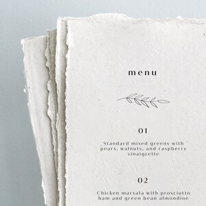 K&ouml;nnte beinhalten: Eine einfache Speisekarte mit handschriftlicher Schrift auf einem strukturierten Papierhintergrund. Die Speisekarte listet zwei Gerichte auf: Standard-Gemischter Salat mit Birnen, Waln&uuml;ssen und Himbeer-Vinaigrette und H&auml;hnchen Marsala mit Prosciutto-Schinken und gr&uuml;nen Bohnen mit Mandel.