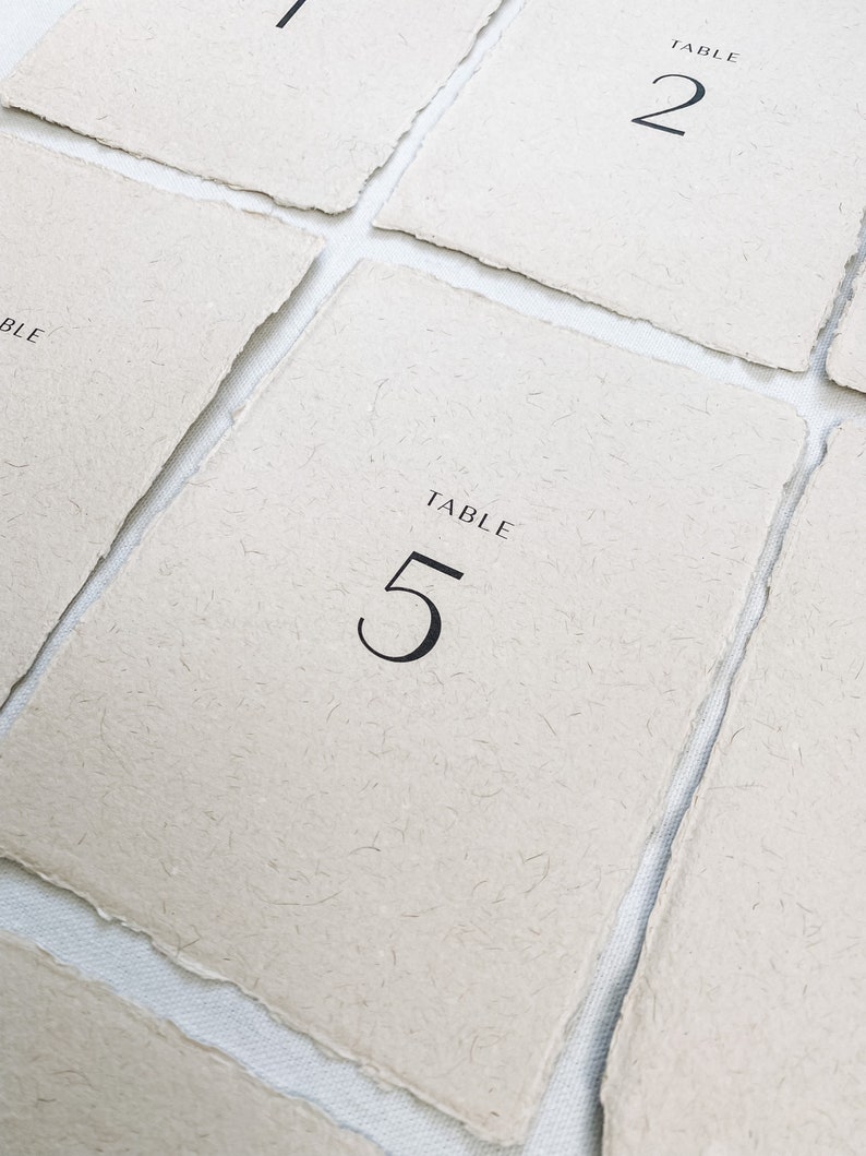 May include: Five table number cards with a rustic, textured paper finish. The cards are labeled "TABLE" and numbered 1, 2, and 5.