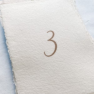 May include: A stack of white paper cards with the number "3" printed in brown ink.