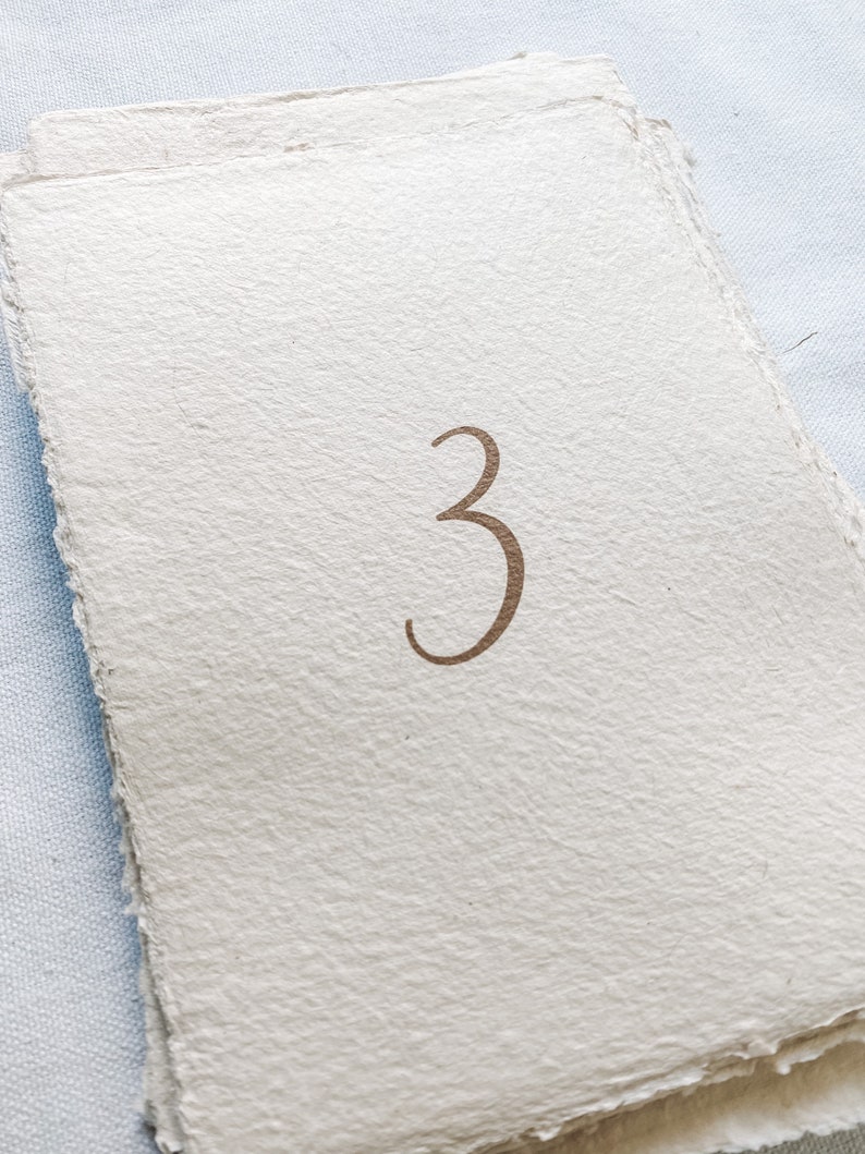 May include: A stack of white paper cards with the number "3" printed in brown ink.