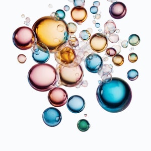 May include: A collection of colorful, iridescent bubbles floating in mid-air against a white background. The bubbles are various sizes and shapes, with some appearing to be overlapping.