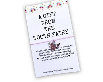 May include: A pink and white card with a tooth fairy charm attached to a pink string. The card reads "A Gift From The Tooth Fairy" and includes instructions for making a wish with the charm.