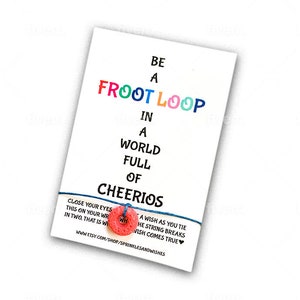 May include: A colorful string bracelet with the text "Be a Froot Loop in a world full of Cheerios" and a red and white wish charm. The text "A wish as you tie the string breaks wish comes true" is also included.