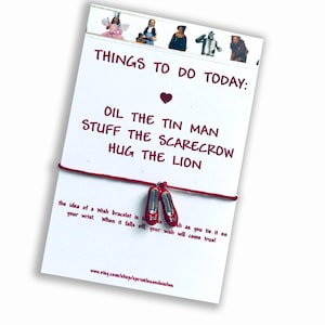 May include: Red and silver wish bracelet with a charm of ruby slippers. The card reads "Things to do today: Oil the Tin Man, Stuff the Scarecrow, Hug the Lion".