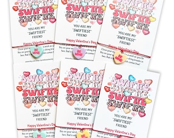 Puede incluir: Seis tarjetas del Día de San Valentín con un brazalete de cuerda roja unido a cada una. El brazalete tiene un dije que dice "Be Mine". Las tarjetas tienen un diseño rosa y blanco con el texto "You are my "Swiftiest" Friend" y "Happy Valentine's Day".