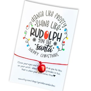 May include: Red string bracelet with a red bell charm and a white card with the text "Dance like Frosty, Shine like Rudolph, Give like Santa. Merry Christmas." and the website address www.etsy.com/shop/sprinklesandwishes.