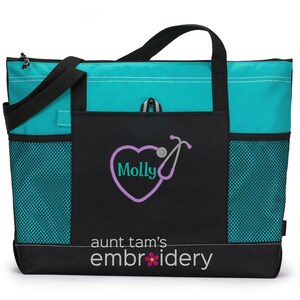 Puede incluir: Un bolso tote turquesa y negro con asas y bolsillos laterales negros. La parte delantera presenta un dise&ntilde;o de estetoscopio en forma de coraz&oacute;n con el nombre "Molly" y el texto "aunt tam's embroidery". La bolsa est&aacute; dise&ntilde;ada para transportar art&iacute;culos.
