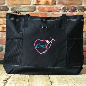 Puede incluir: Bolso tote negro con costuras blancas y bolsillos laterales de malla. El bolsillo delantero presenta un dise&ntilde;o de estetoscopio en forma de coraz&oacute;n rosa con el nombre "Joni" en turquesa y "CNA" en blanco. El bolso tiene asas negras.
