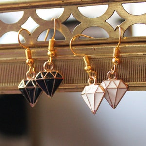 Puede incluir: Un par de pendientes de oro con dijes en forma de diamante. Un dije es negro y el otro es blanco.